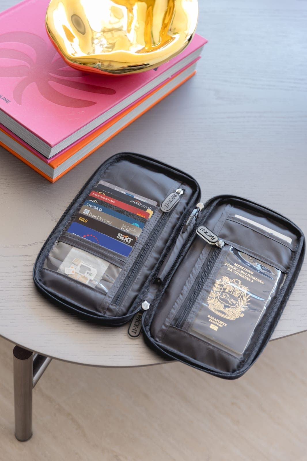 Passport Holder gris abierto sobre una mesa de madera gris, con tarjetas de crédito en un lado y un pasaporte venezolano en el bolsillo…