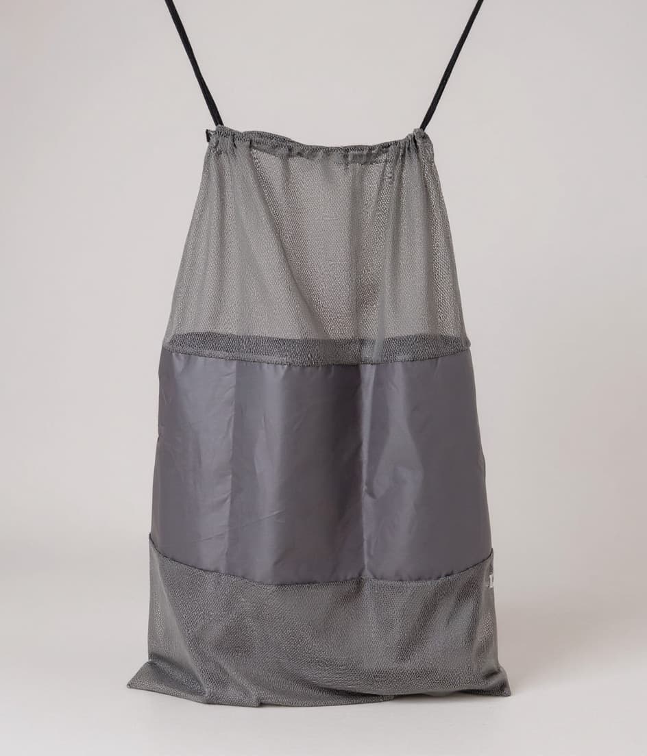 Laundry Bag gris de malla con cordón negro, colgada de frente sobre fondo claro